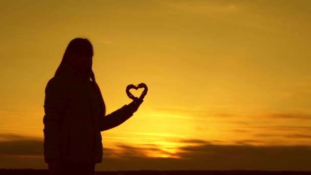 einsame Silhouette eines Mädchens, das ein Herz auf einem schönen Sonnenuntergang und der hellen Sonne hält. - Filmmaterial, Video