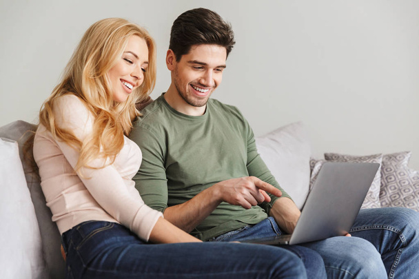 Cute young loving couple sitting on sofa using laptop computer. - 写真・画像