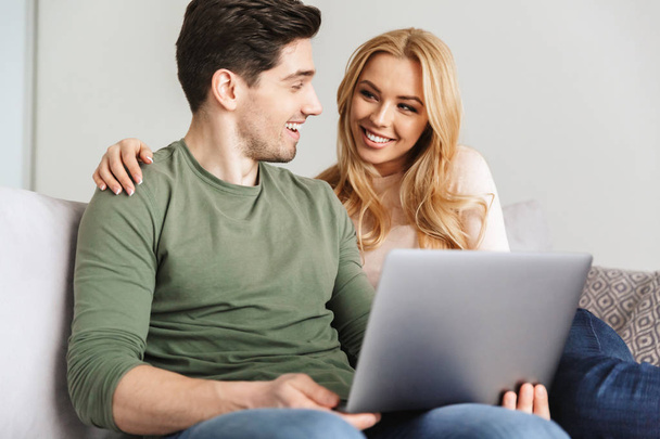 Cute young loving couple sitting on sofa using laptop computer. - Foto, Imagen