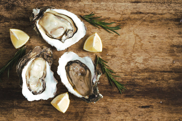 verse net geopend oesters en plakjes citroen op rustieke houten achtergrond - Foto, afbeelding