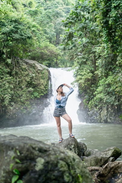 женщина, стоящая на скале с водопадом Aling-Aling и зелеными растениями на заднем плане, Бали, Индонезия
 - Фото, изображение