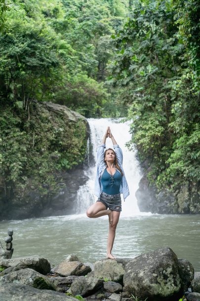 attractive woman practicing yoga with Aling-Aling waterfall on backdrop, Bali, Indonesia - Photo, Image