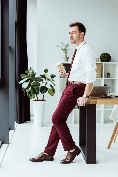 thoughtful businessman with coffee to go leaning on table with laptop - Foto, imagen