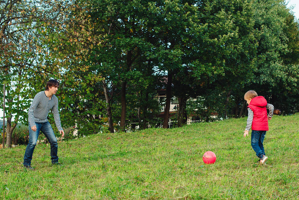 Joven padre con su pequeño hijo jugando al fútbol en el césped verde
. - Foto, imagen