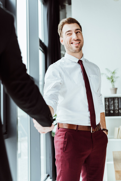 businessman winking and shaking hands with colleague in office - Photo, Image