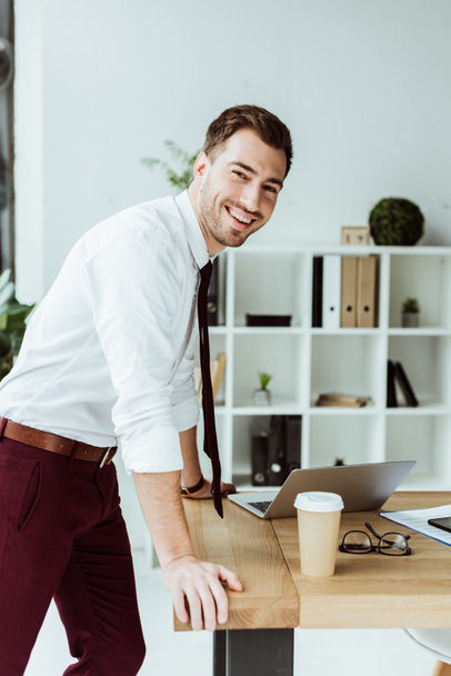 ευτυχής επιχειρηματίας στέκεται στο χώρο εργασίας με φορητό υπολογιστή και καφέ να πάει - Φωτογραφία, εικόνα