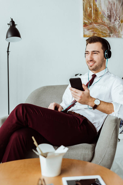 красивий бізнесмен слухає музику в навушниках і використовує смартфон в офісі
 - Фото, зображення