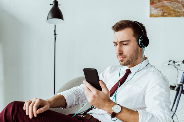 handsome businessman listening music in headphones and using smartphone - Foto, imagen