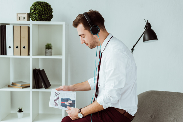 handsome businessman listening music in headphones and reading newspaper - Photo, Image