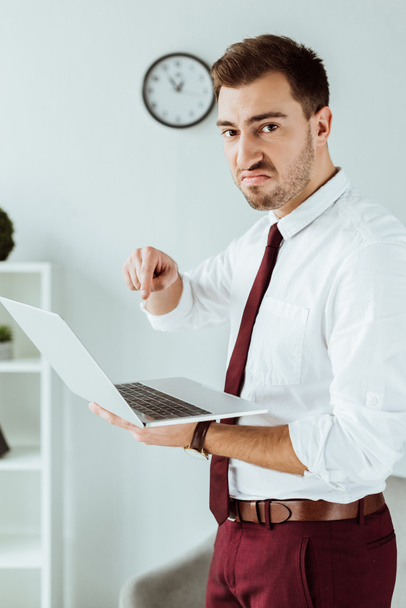сердитий бізнесмен вказує на ноутбук в сучасному офісі
 - Фото, зображення