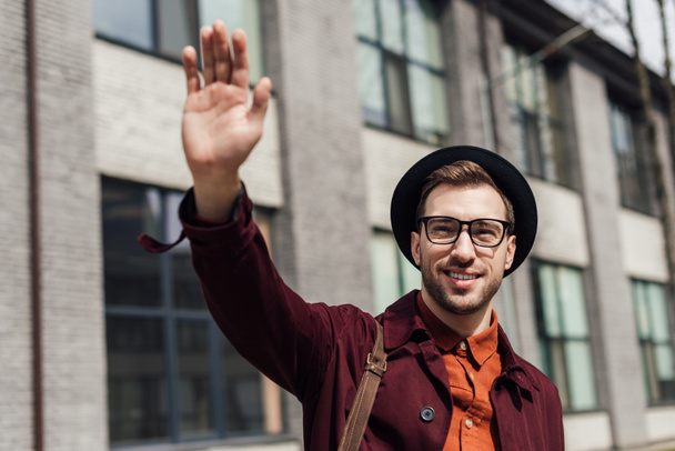 stylish young man in glasses and hat waving to someone  - Foto, Bild