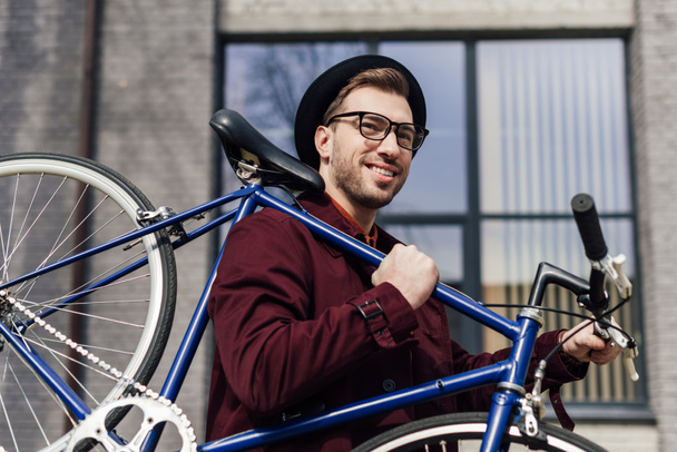 handsome trendy man carrying bike on shoulder - Valokuva, kuva