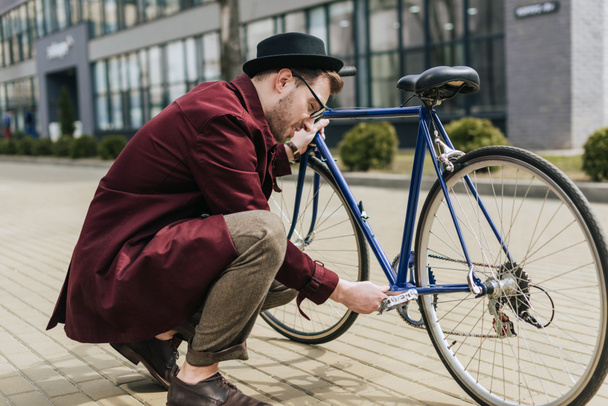 handsome stylish man repairing bicycle on street - 写真・画像