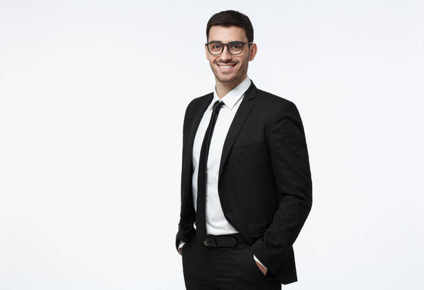 Indoor picture of young business man in glasses pictured isolated on grey background looking straight at camera, showing confidence and providing stability for employees - Foto, imagen