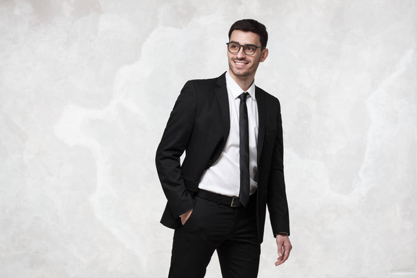 Elegant smiling young business man walking against grey texture wall - Foto, Imagen