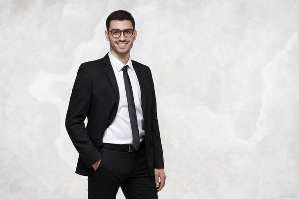 Elegant smiling young business man standing against grey texture wall - Fotó, kép