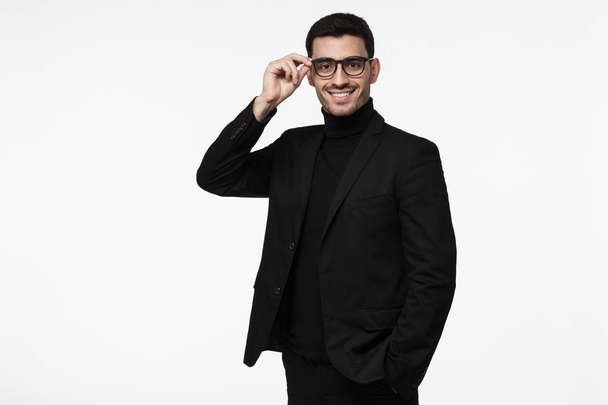 Contemporary intelligent business man wearing black suit holding his spectacles, isolated grey background - Foto, afbeelding