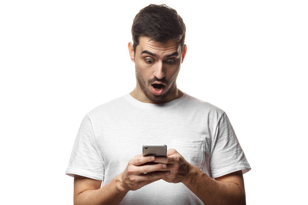 Portrait of young man isolated on white background, looking agitated at display of her smartphone, impressed by media content from web - Foto, Imagem