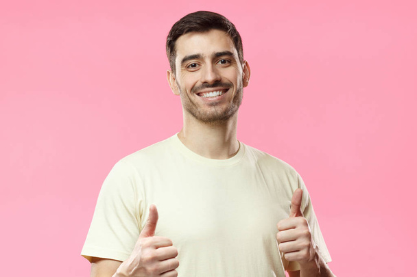 Young optimistic man isolated on pink background showing thumbs up with positive emotions of content and happiness. Concept of satisfaction with quality and recommendation - Фото, зображення