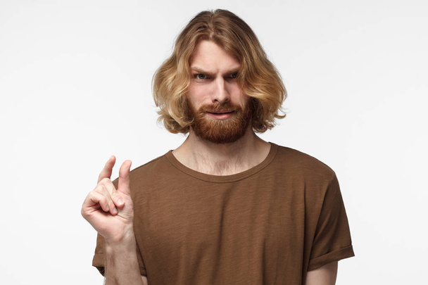 Young bearded man in brown tshirt, gesticulates with hands, showing little size with unpleased face expression. So tiny!  - 写真・画像