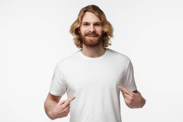 Smiling nice man pointing at his blank white tshirt with both index fingers, copy space for your advertising, isolated on grey background - Photo, image