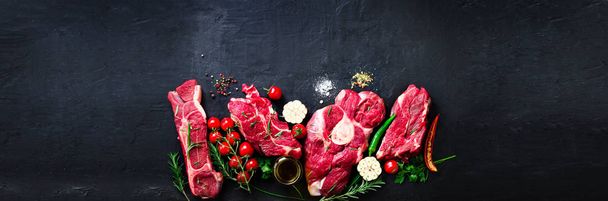 Raw fresh meat steak with cherry tomatoes, hot pepper, garlic, oil and herbs on dark stone, concrete background. Banner. - Zdjęcie, obraz