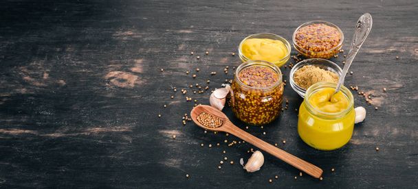 Assortment of mustard in sauces. Spices On a black wooden background. Top view. Copy space for your text. - Fotografie, Obrázek