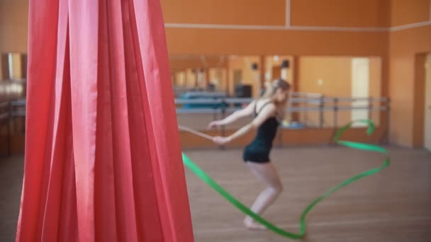 Young attractive woman trains with a green ribbon - gymnastics exercise in studio with mirror - de-focused - Footage, Video