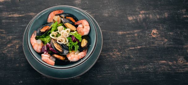 A plate of seafood. Mussels, squid, shrimp. Top view. On a black wooden background. Copy space. - Foto, Imagem