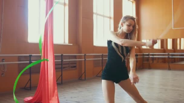 Young attractive woman trains with a green ribbon - gymnastics exercise in studio with mirror - Imágenes, Vídeo