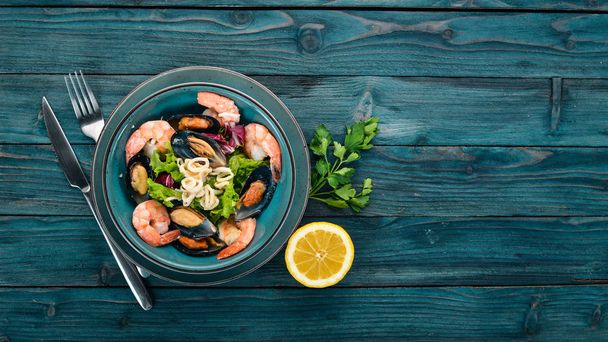 A plate of seafood. Mussels, squid, shrimp. Top view. On a blue wooden background. Copy space. - Photo, Image