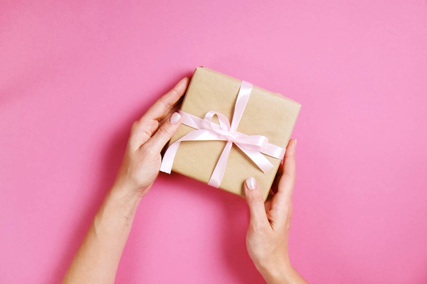 Close up of female hands holding birthday gift in vintage craft paper wrapping. Femenine composition with present in woman's arms. - Zdjęcie, obraz
