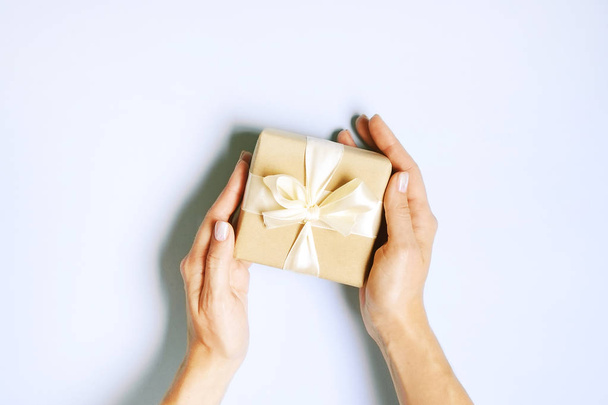 Close up of female hands holding birthday gift in vintage craft paper wrapping. Femenine composition with present in woman's arms. - Фото, изображение