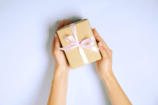 Close up of female hands holding birthday gift in vintage craft paper wrapping. Femenine composition with present in woman's arms. - Фото, изображение
