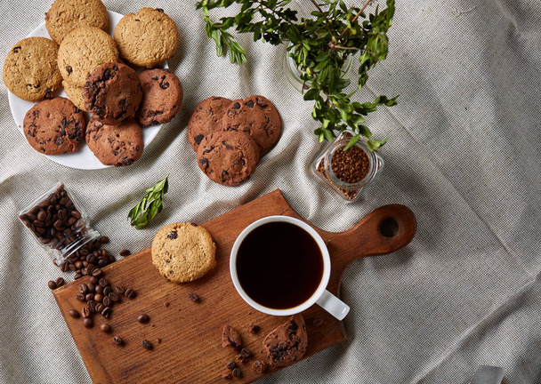 Coffee cup, jar with coffee beans, cookies over rustic background, selective focus, close-up, top view - Fotografie, Obrázek
