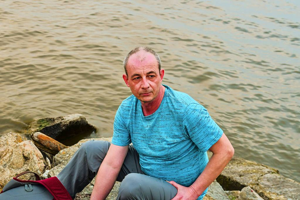 Uomo di mezza età seduto sulla riva del lago. Solitudine uomo maturo seduto sulla riva. Concetto di solitudine
 - Foto, immagini