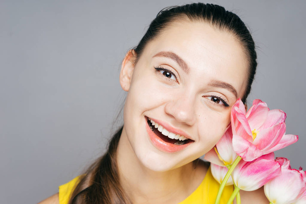 happy smiling girl in a yellow dress laughing and holding a fragrant pink flower - Photo, Image