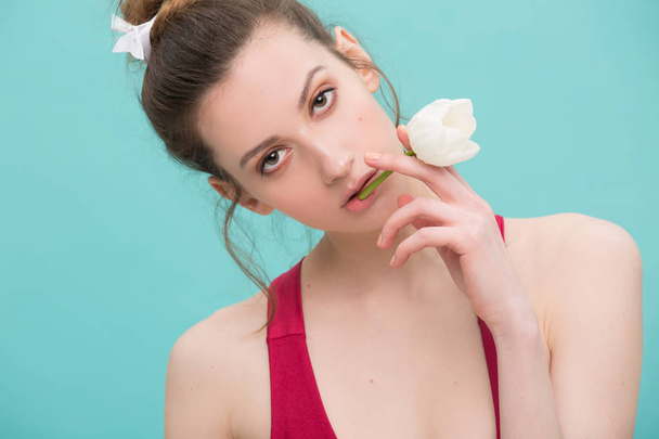 Close up sexy model in red swimsuit holding white tulip and smoking flower as a cigarette over mint colour background. Beautiful fashion girl with a flower on her lips. Conseptual photo - Фото, изображение