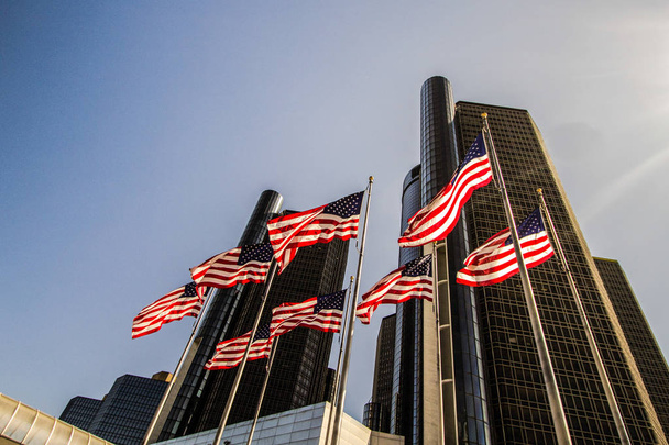 Detroit, Michigan, USA - March 18, 2018: American Flags fly in front of the Detroit Renaissance Center in the downtown district. The skyscraper is the world headquarters of the General Motors Corporation - Foto, imagen