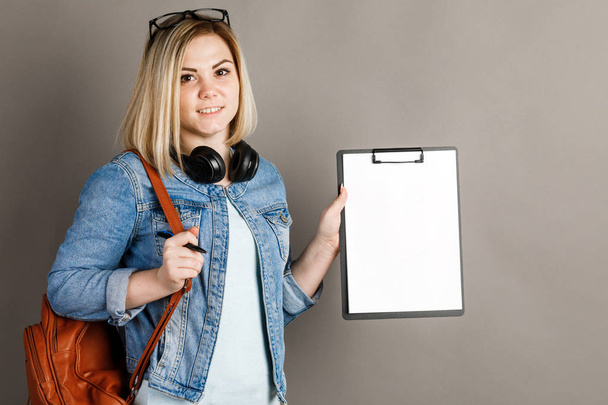 Een student-vrouw houdt een schoolbord op een grijze achtergrond. vrouw en manier van leven - Foto, afbeelding