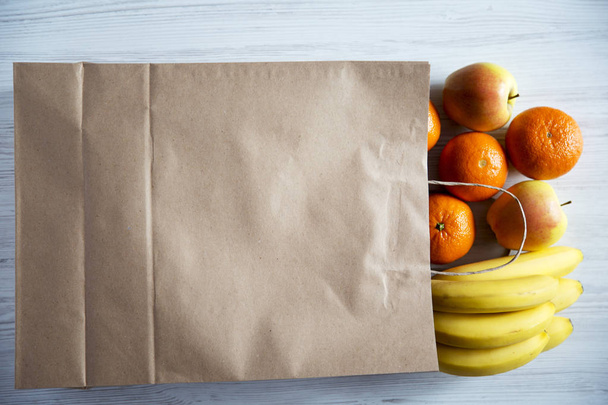 Бумажный пакет из различных фруктов и хлеба на белом деревянном фоне. Плоский лежал. Вид сверху
. - Фото, изображение
