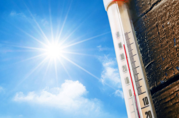 Thermometer mit einer Hochtemperaturanzeige auf einer Skala, vor dem Hintergrund der strahlenden Sonne und eines blauen Himmels mit Wolken. Das Konzept von heißem, gefährlichem Wetter, globaler Erwärmung. - Foto, Bild