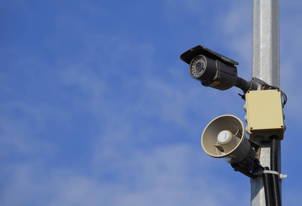 CCTV camera and loudspeaker alarm on a pole against a blue sky. - Foto, afbeelding