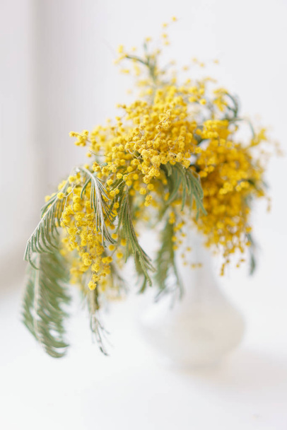 Belos ramos de mimosa em vaso de vidro no peitoril da janela. Flores amarelas ensolaradas na mesa branca perto da janela - Foto, Imagem