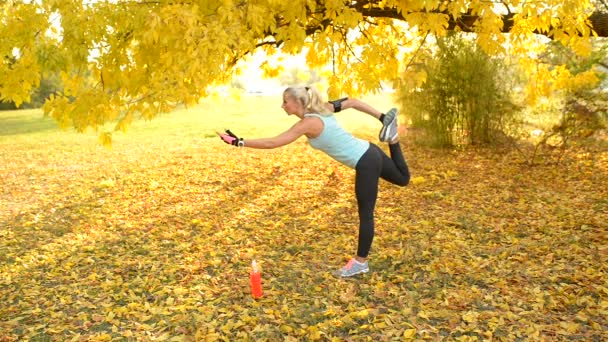 Vonzó nő, nyúlik a lábát a földön borított levelek, nyilvános parkban. Egészséges életmód fogalma. - Felvétel, videó