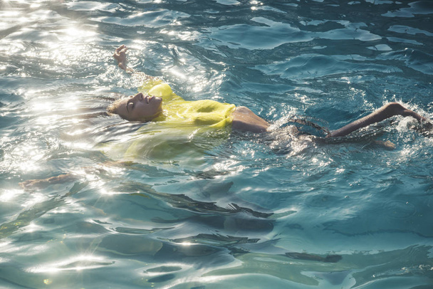 Beautiful young woman in sexy yellow dress swimming at sea beach - Foto, Bild