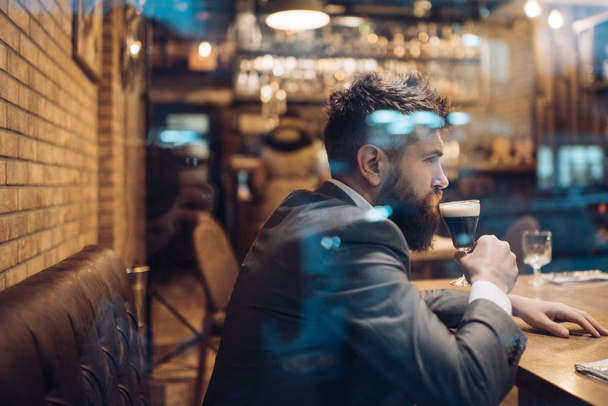 Bearded man rest in restaurant with beer glass. Businessman with long beard drink in cigar club. Beer time. serious bar customer sit in cafe drinking ale. Date meeting of hipster awaiting in pub. - Фото, зображення