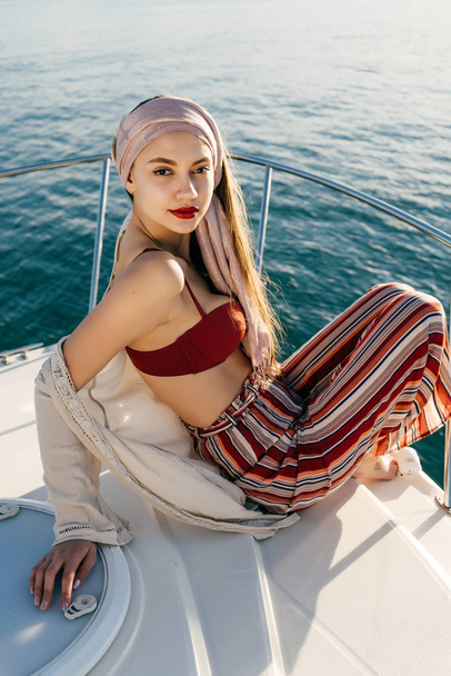 an attractive confident girl in stylish clothes sits on her white yacht, enjoys a rich life and rest - Foto, imagen