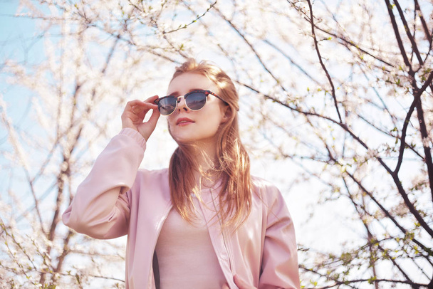 Spring fashion girl outdoors portrait in blooming trees. Beauty Romantic woman in flowers in sunglasses. Sensual Lady. Beautiful Woman Enjoying Spring Nature and fantasy orchard. Blossom girl. Pink . - Фото, изображение