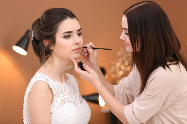 Professionele make-up artist werken met jonge bruid in salon - Foto, afbeelding